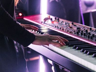 Electronic and Produced Music Students playing the keyboard on stage with a pink hue light in the background